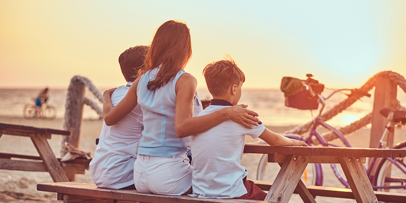 Back view cute family mother with her sons sitting bench looks sunset seacoast